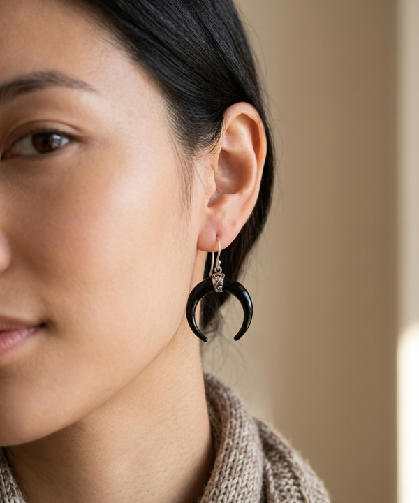 Boucle d'oreille en corne noire en forme de croissant de lune portée, monture en argent ciselé, style bohème chic.
