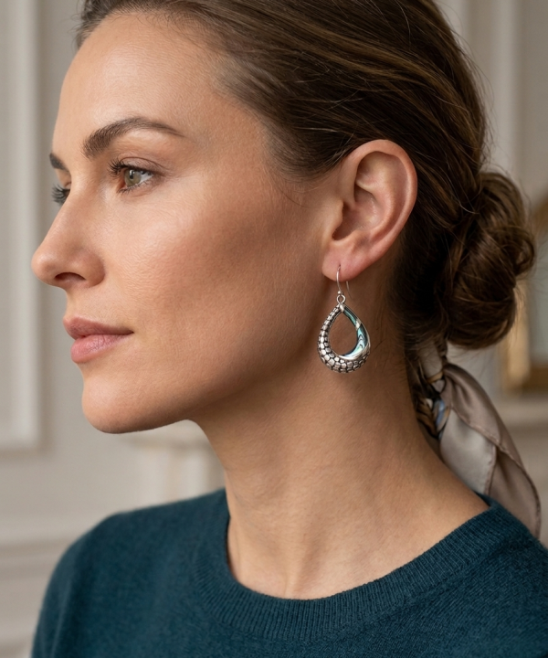 Boucle d'oreille pendante en argent ciselé avec incrustation d'abalone portée par une femme.