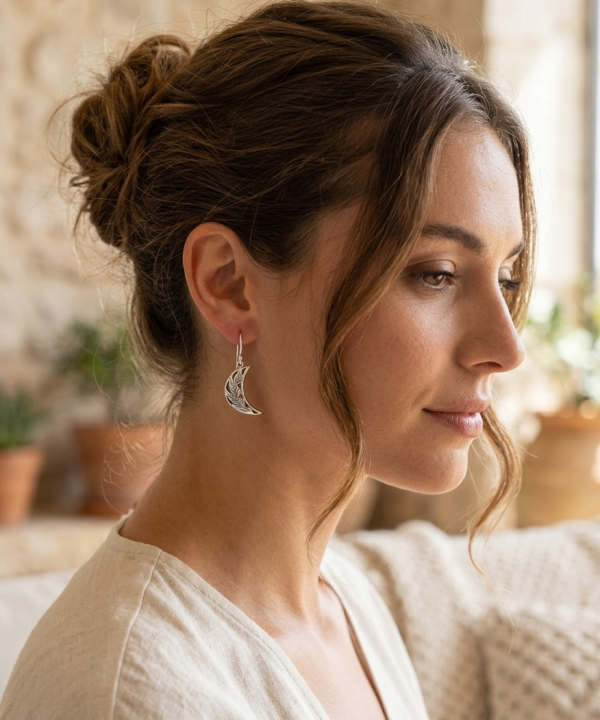 Portrait en profil de droite d'une femme souriante, portant une boucle d'oreille pendante en forme de croissant de lune argenté ornée d'un motif de feuilles.