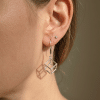 Boucle d'oreille pendante en argent design cube géométrique ajouré portée à l'oreille.