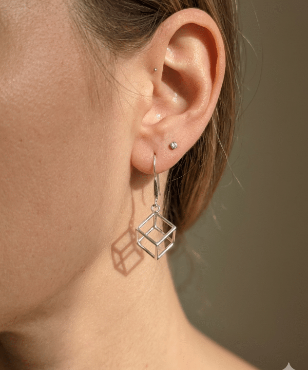 Boucle d'oreille pendante en argent design cube géométrique ajouré portée à l'oreille.