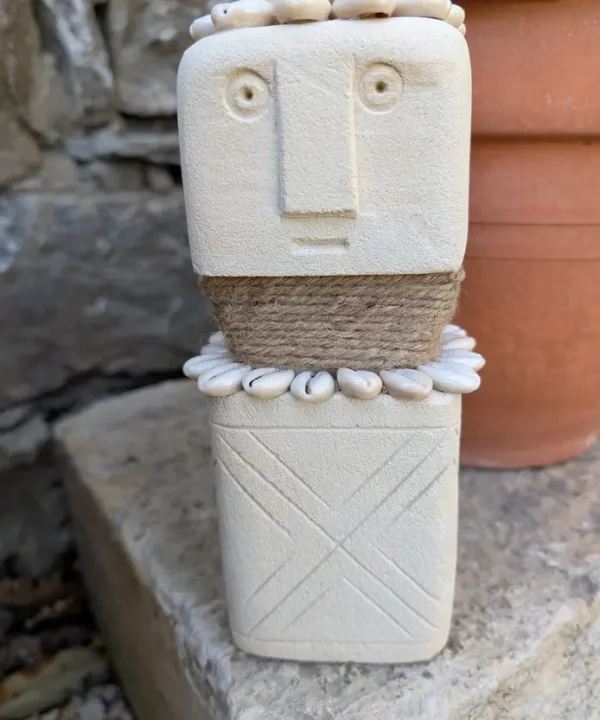 Statuette Sumba artisanale en grès crème, cauris blancs et jute, symbole de protection.