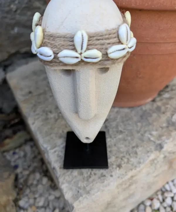 Statuette Sumba artisanale en grès beige, visage tribal avec bandeau cauris sur socle.